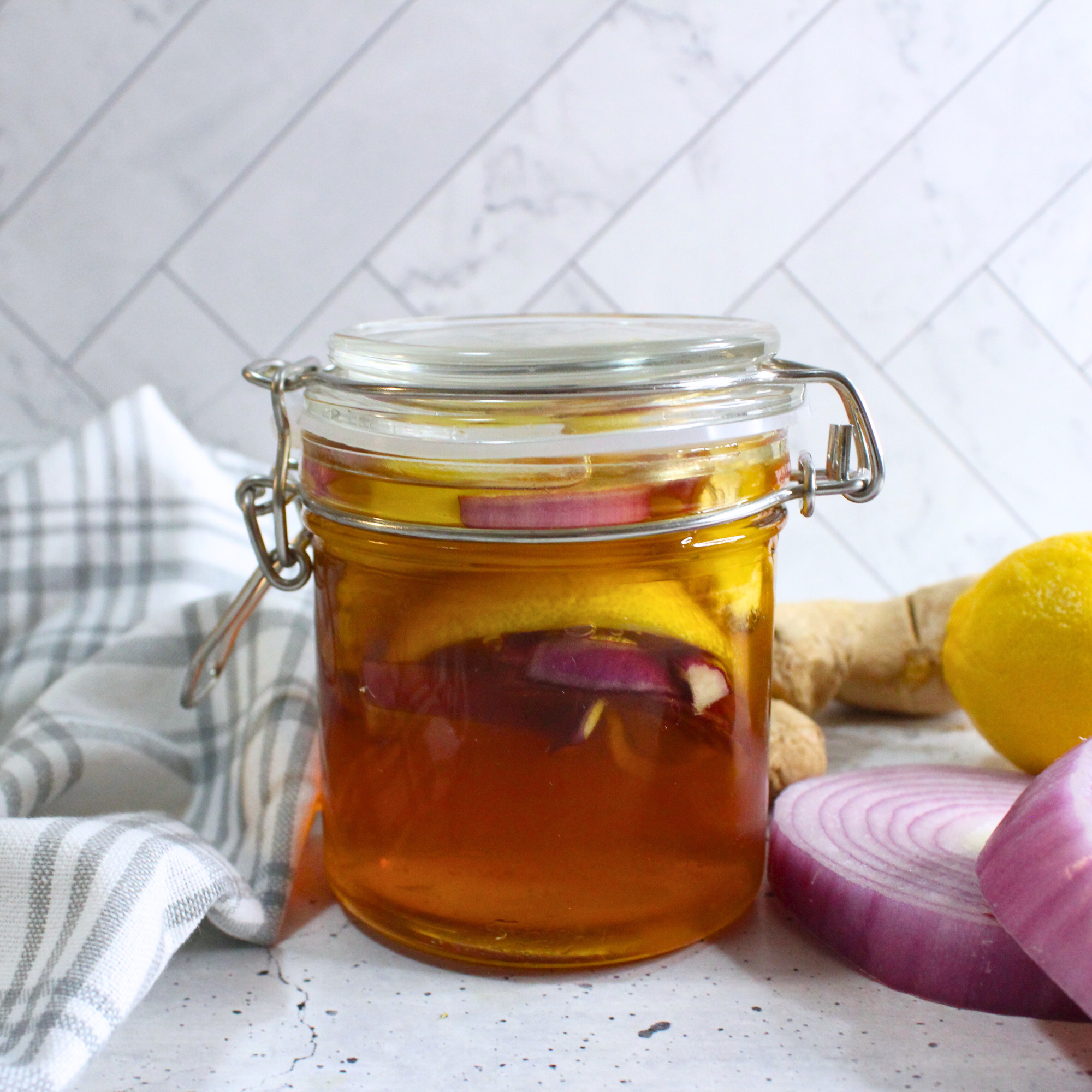 Honey, onion, ginger, and lemon cough syrup in a glass jar on a white counter.