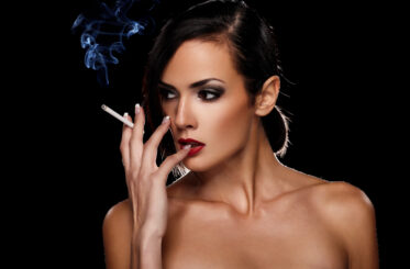 Woman smoking and looking to the side. black background.