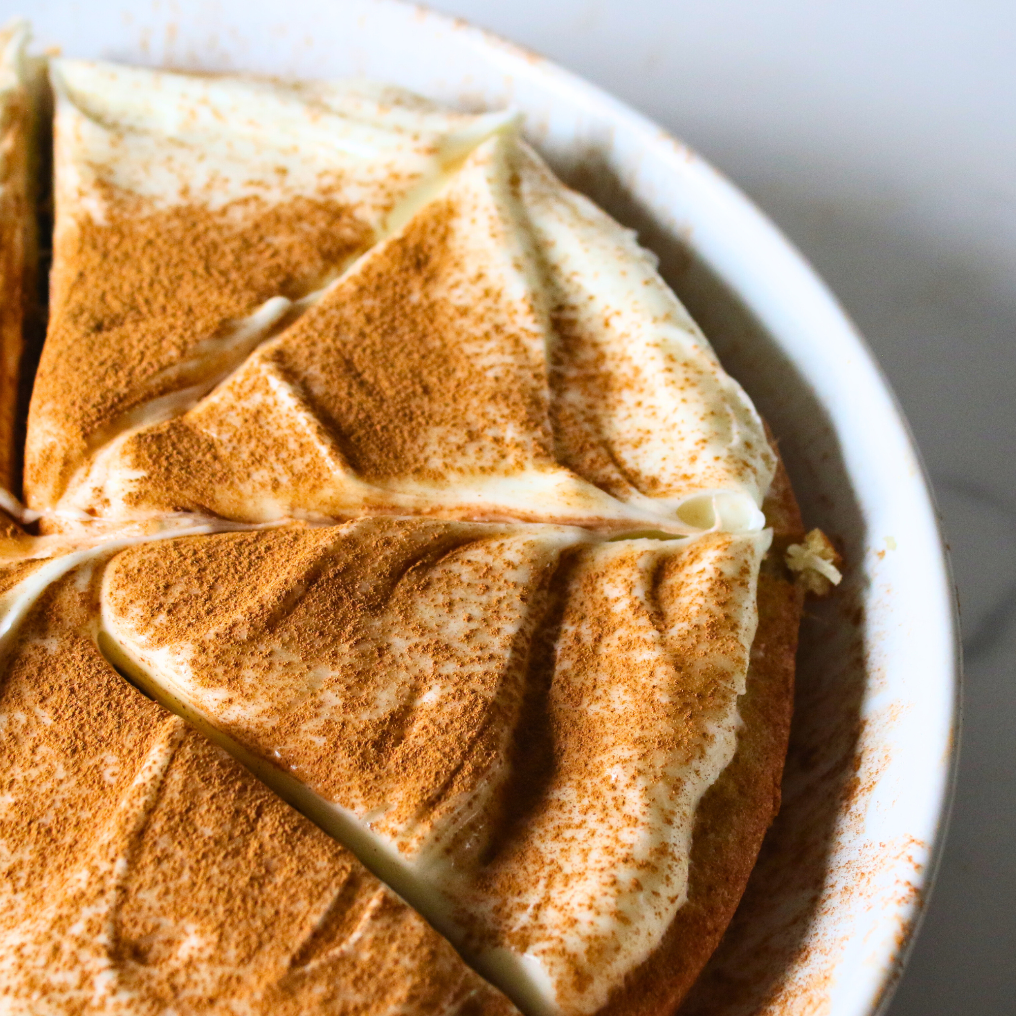 Sliced almond coconut flour cake topped with frosting and cinnamon.