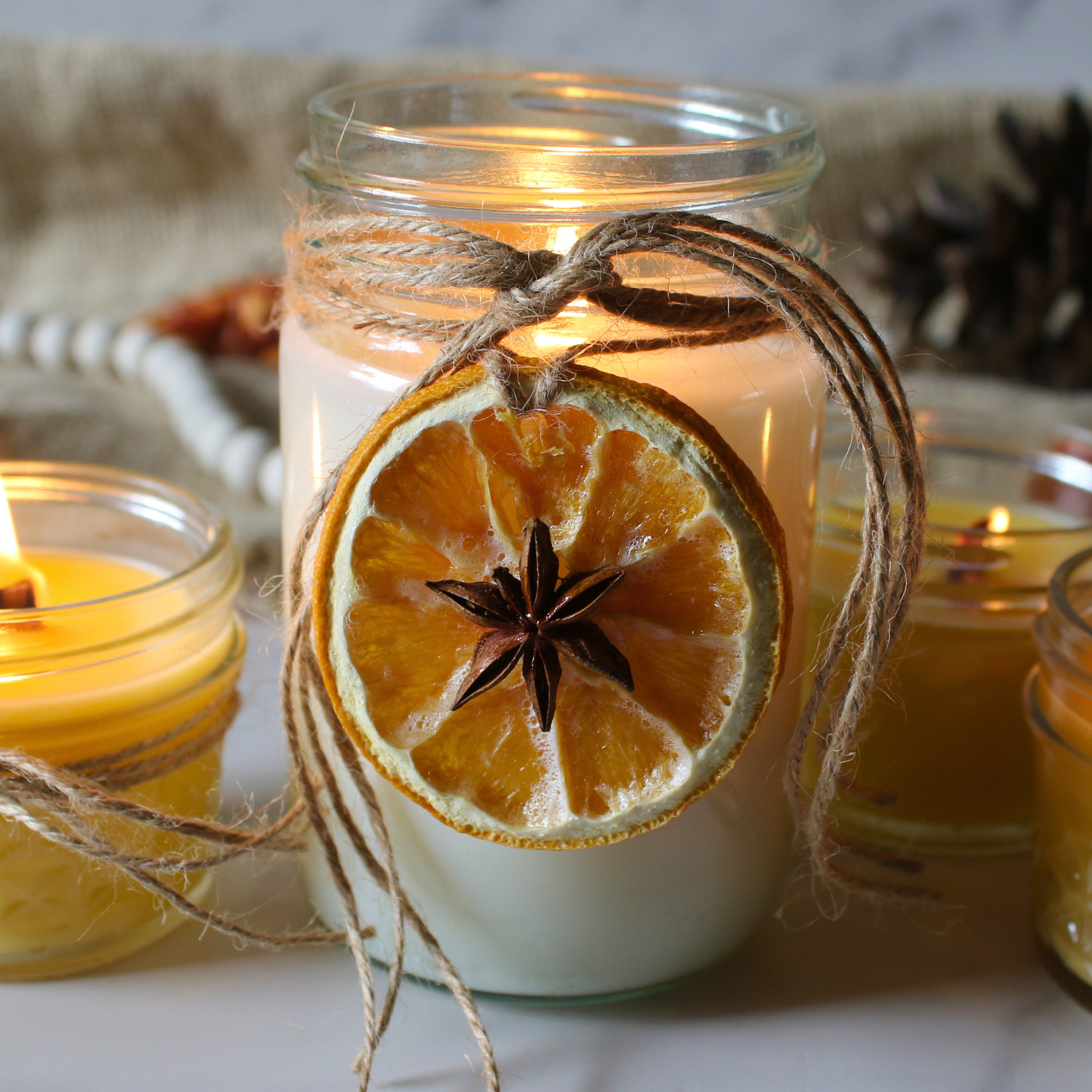 Homemade mason jar candles decorated with twine and dried orange slices.