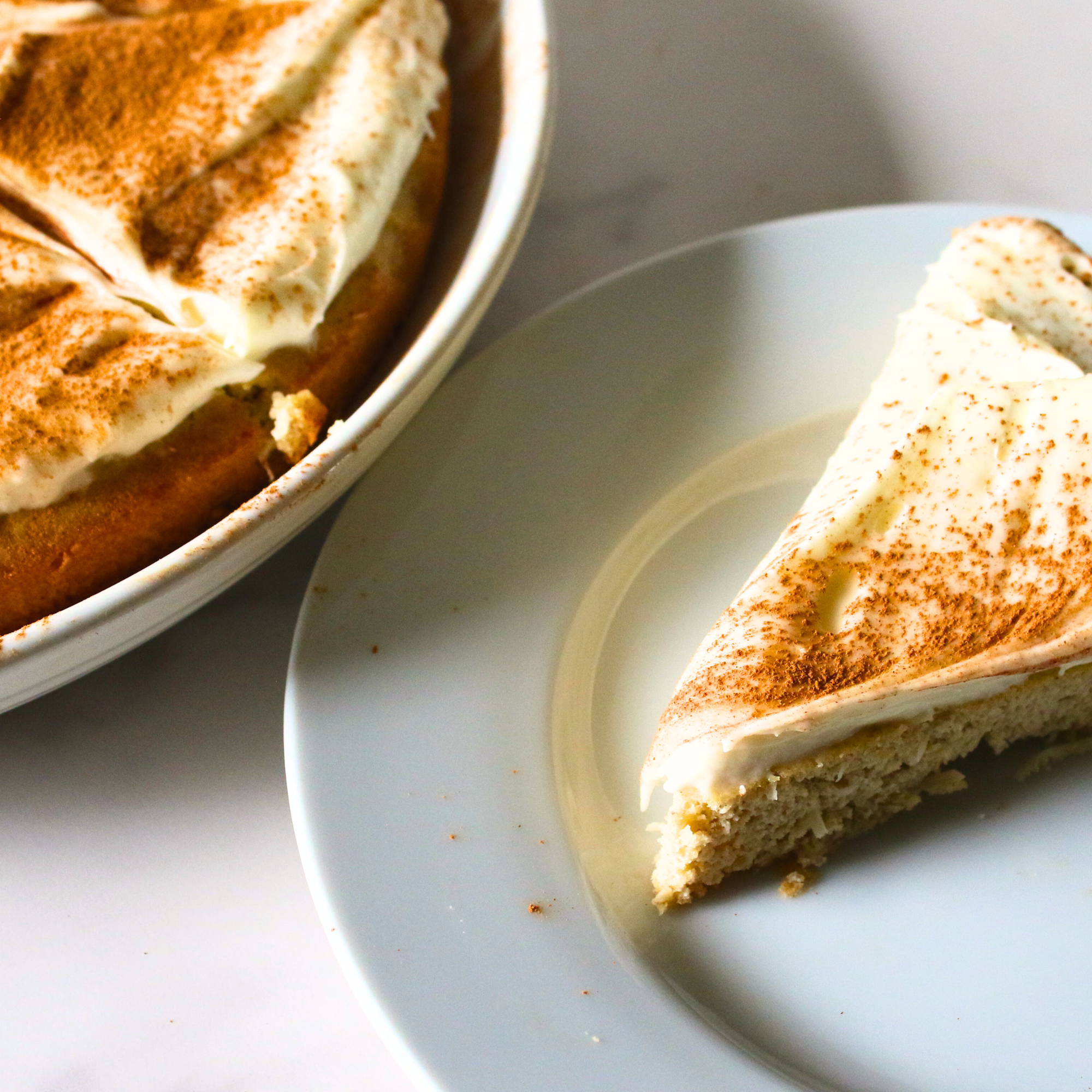 A slice of coconut cake topped with frosting and cinnamon. 