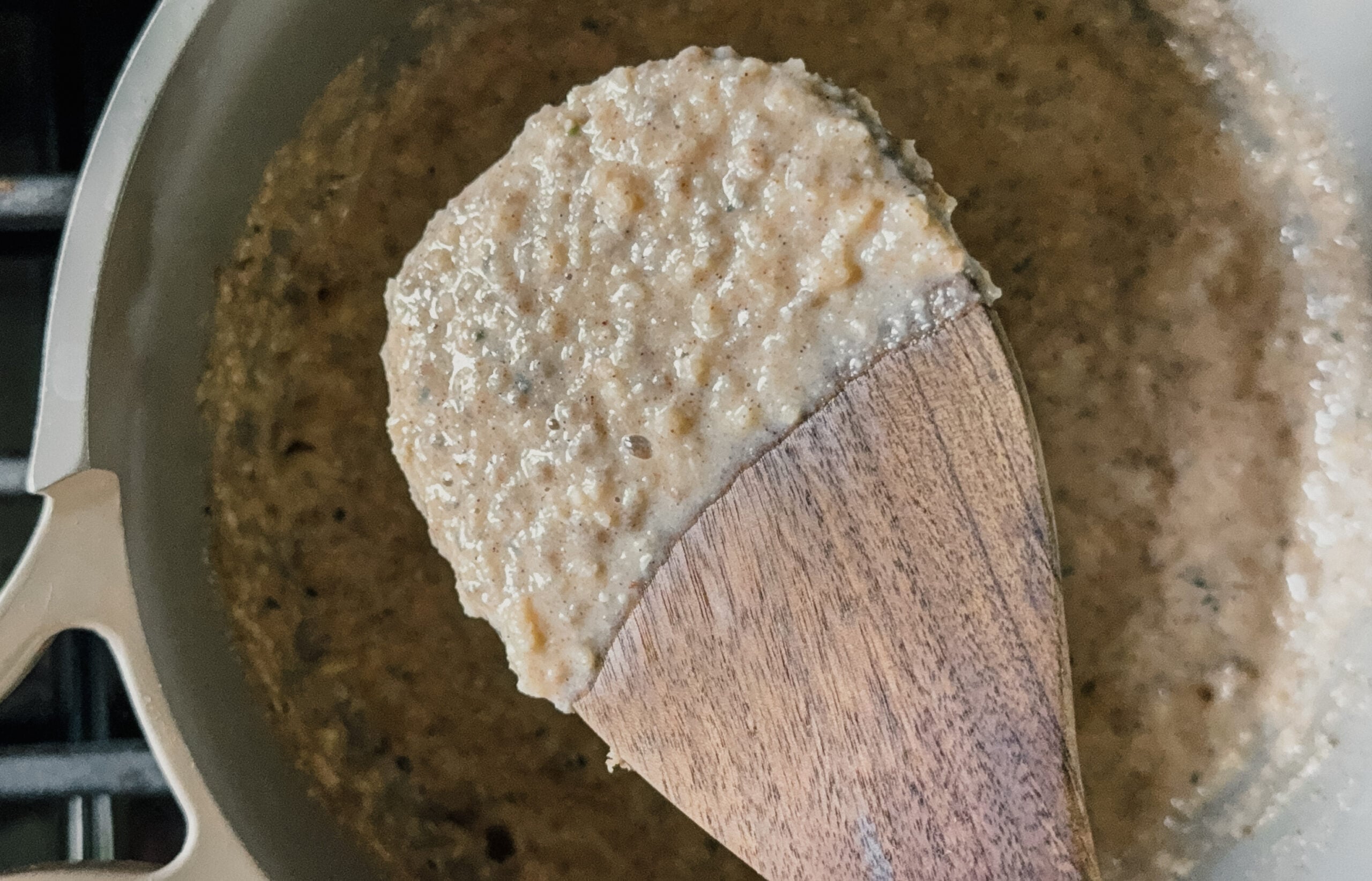 A scoop of cooked oatmeal on a wooden spoon above a pot of the remaining oatmeal.