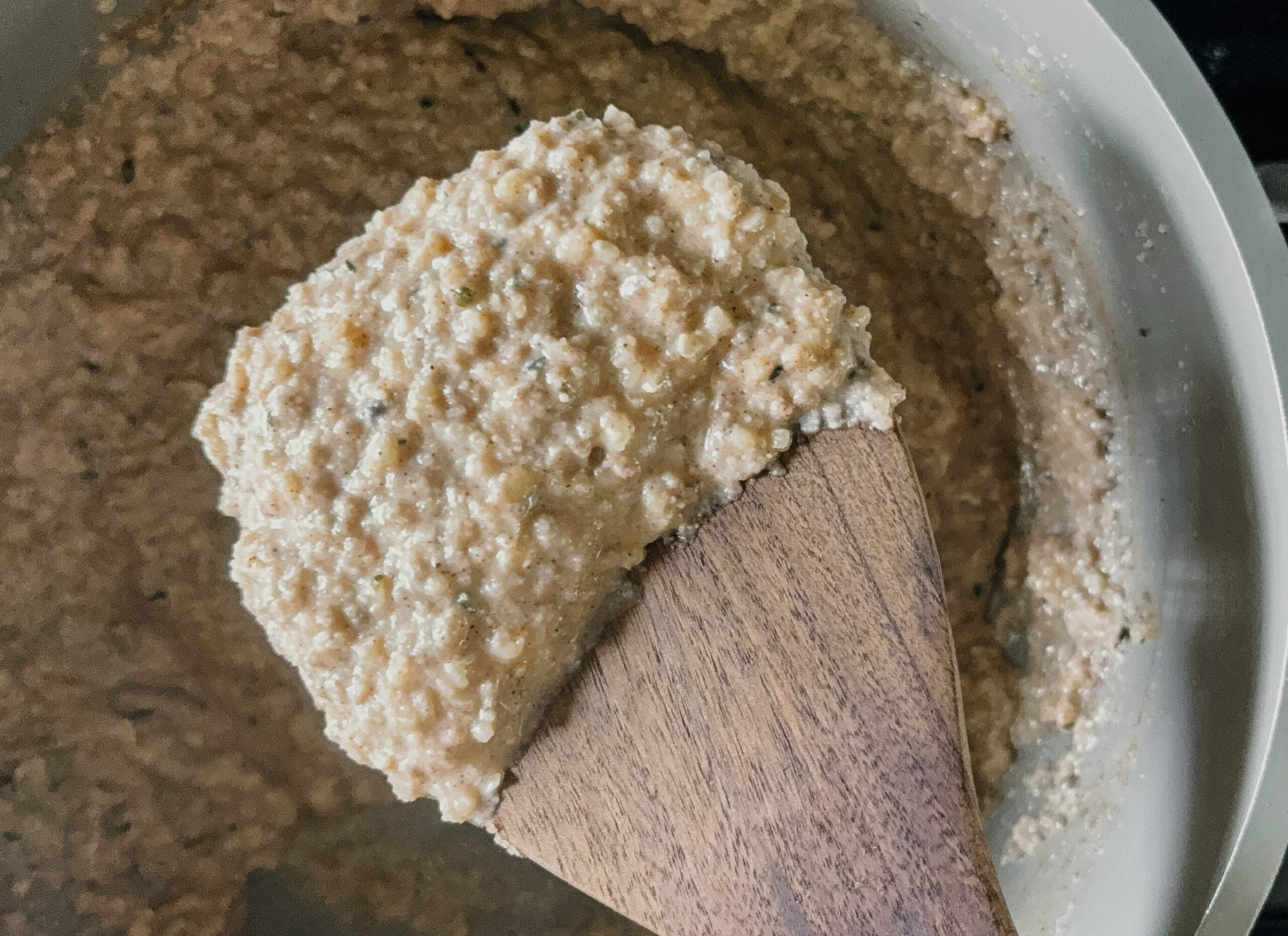 A scoop of cooked oatmeal on a wooden spoon above a pot of the remaining oatmeal.