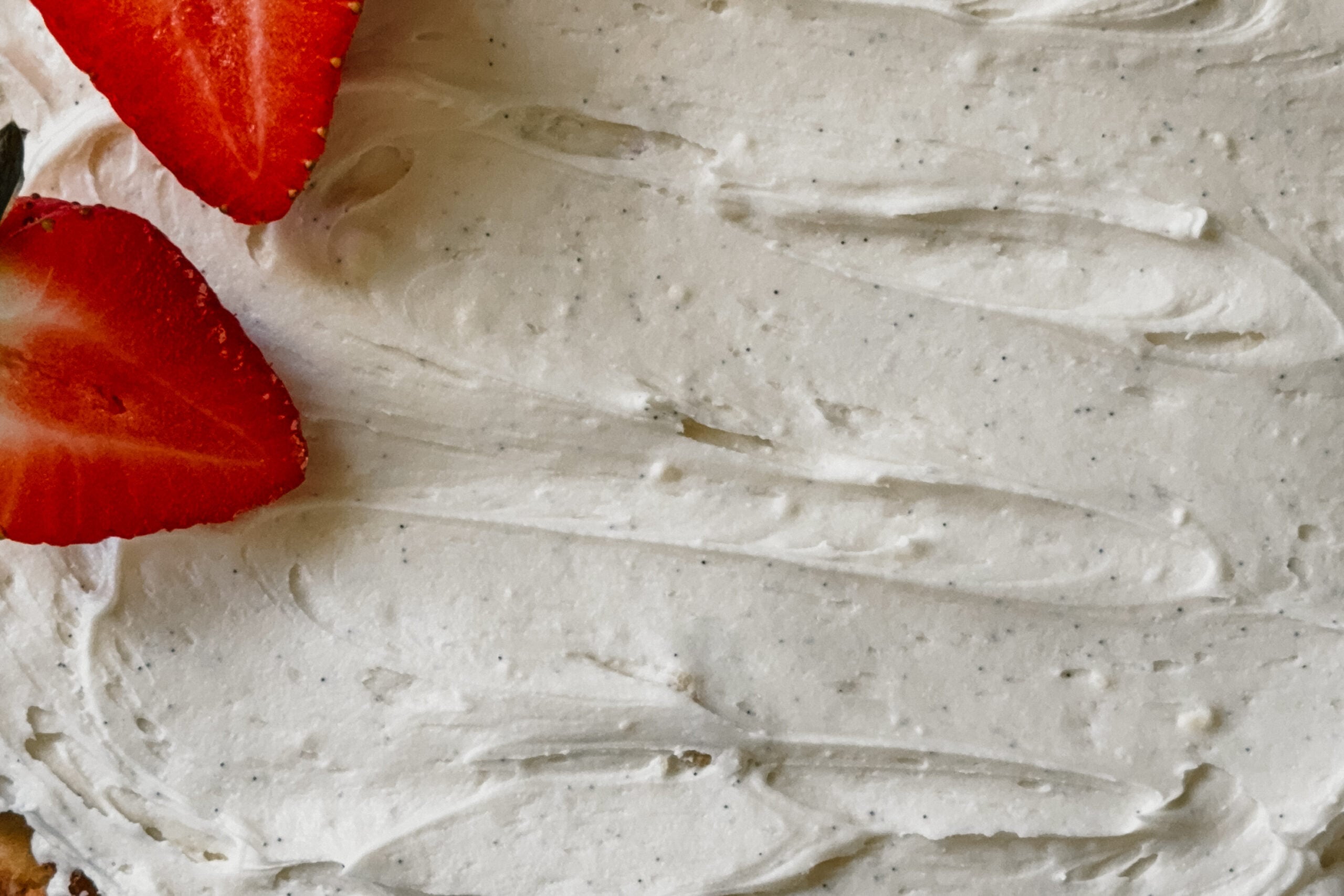 A close up of vanilla bean frosting. Two strawberries are in the upper left corner.