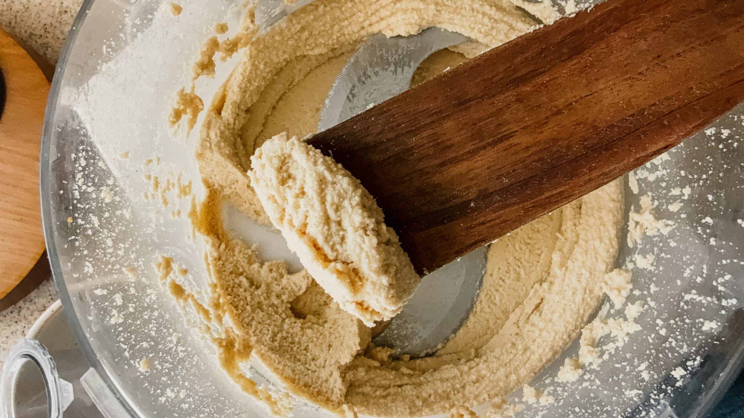 A wooden spatula with a scoop of freshly made peanut butter above a food processor.
