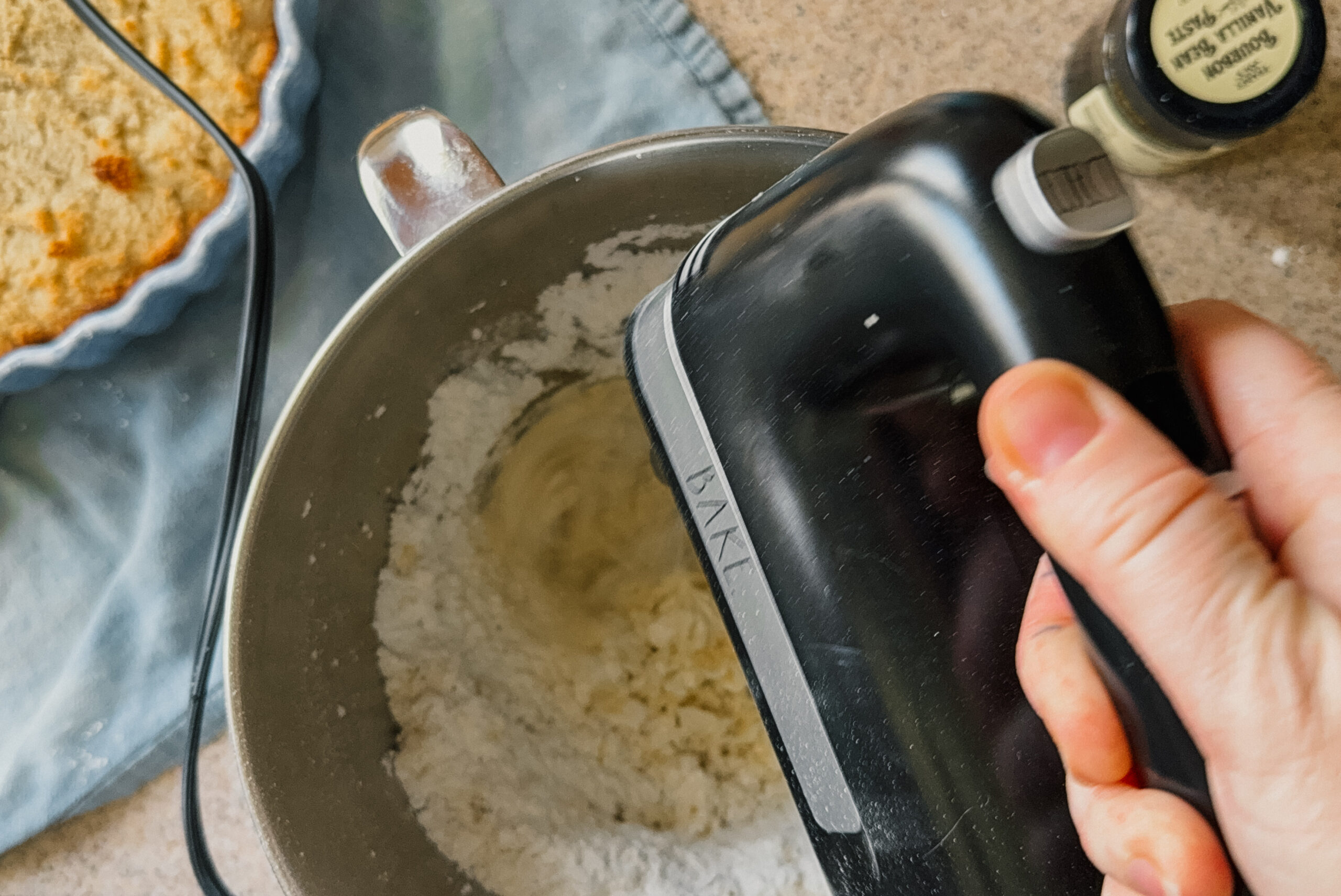 A hand mixer whipping frosting ingredients in a silver bowl.
