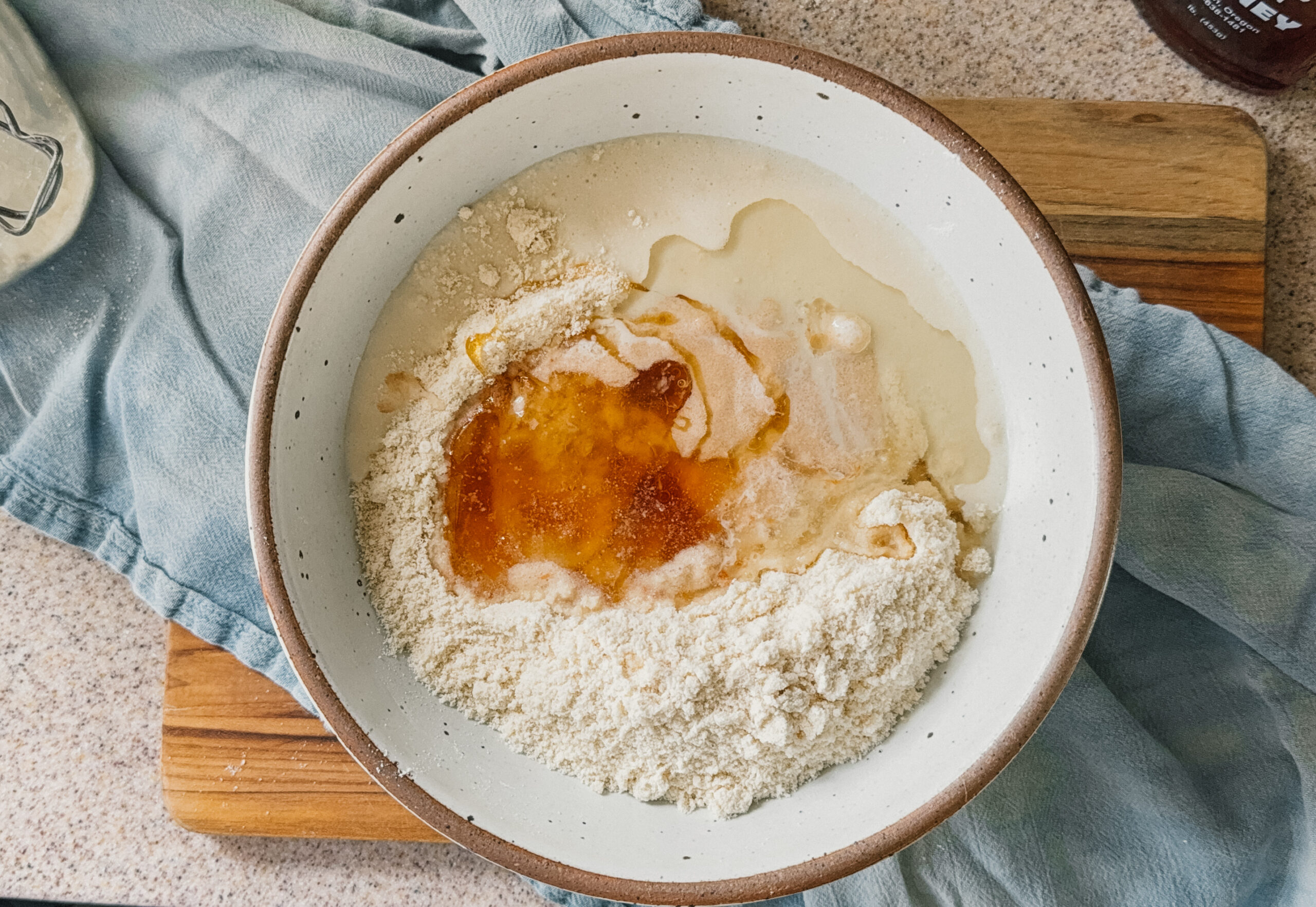 A bowl of ingredients about to be mixed. A blue tea towel and wooden board are underneath the bowl.