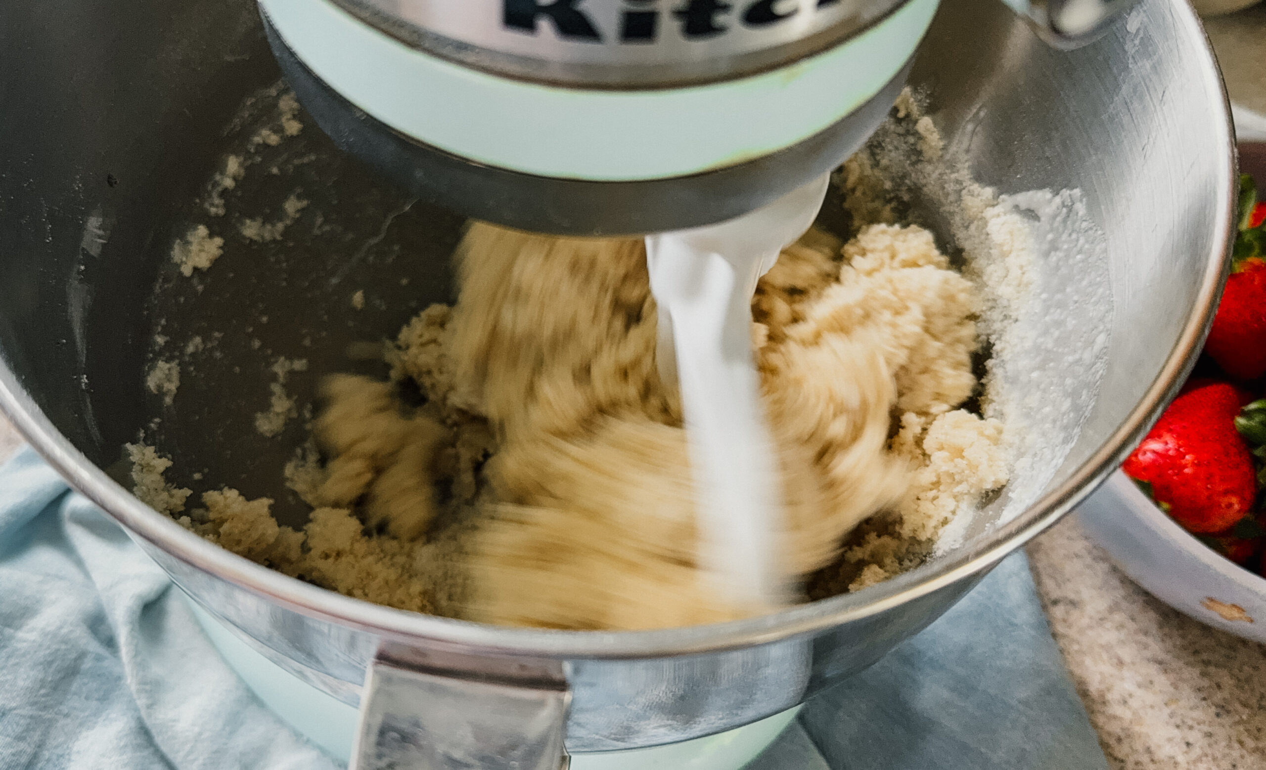 A close up of a mixer whipping ingredients together. A blue tea towel is underneath the mixer.
