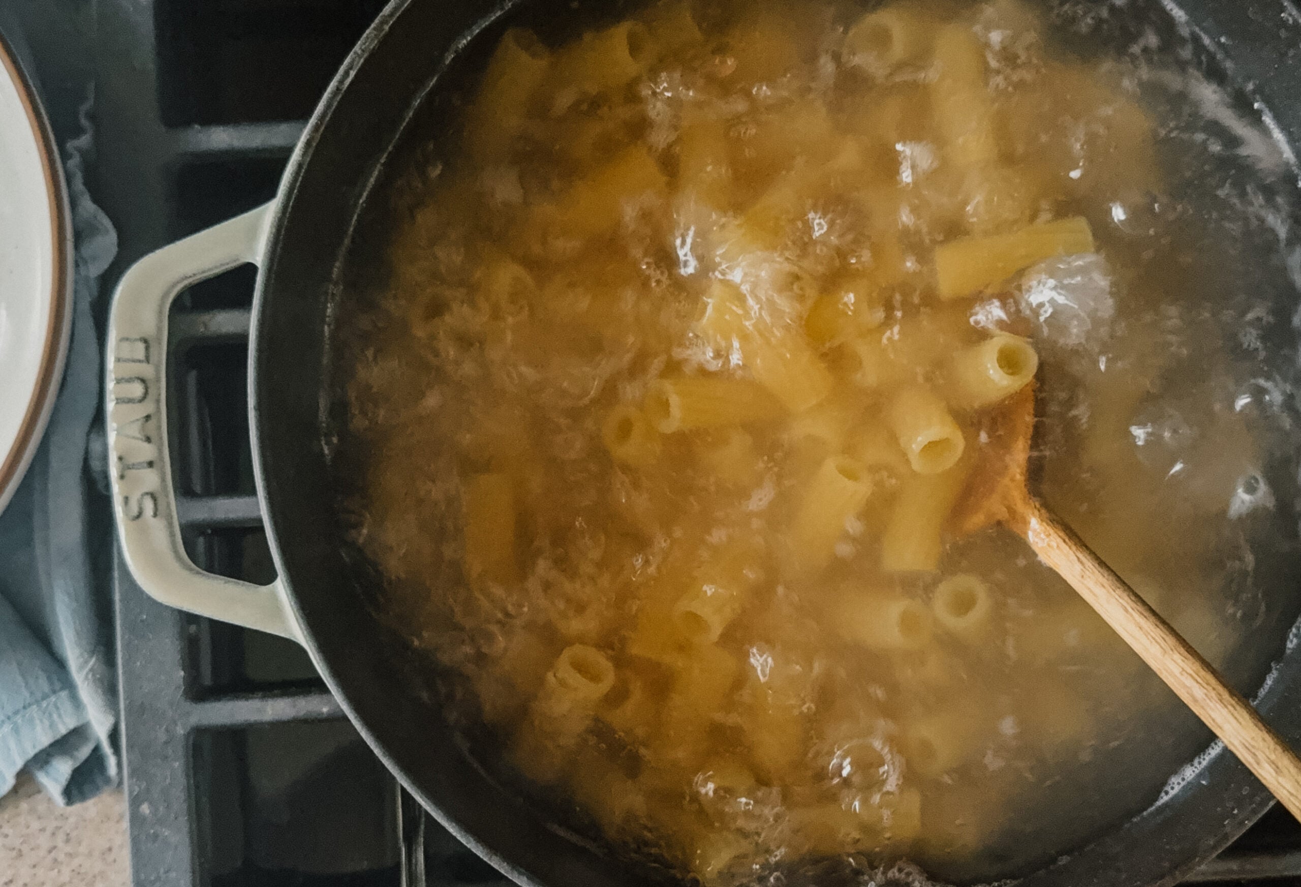 A large pot of cooking pasta with a wooden spoon sticking out towards the bottom right.