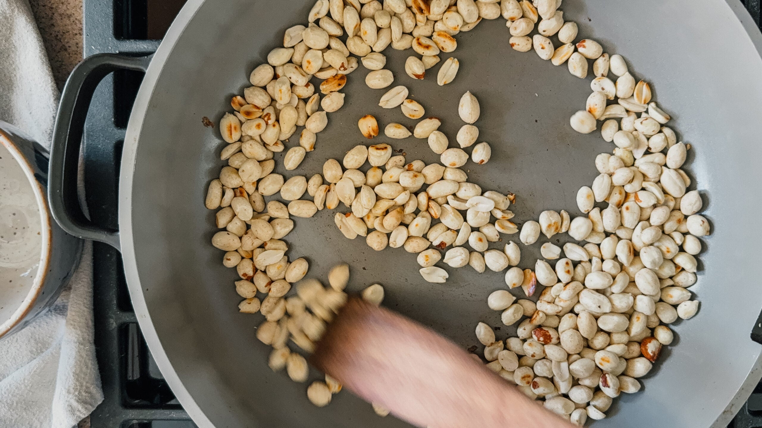 Peanuts being actively roasted in a pan, being stirred by a wooden spatula.