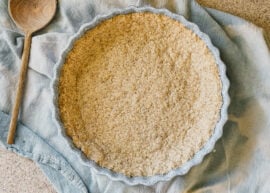 A freshly baked pie crust in a blue pie dish. The dish sits on top of a blue tea towel.