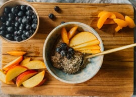 A bowl of almond flour porridge surrounded by fresh fruits. A golden spoon rests to the bottom right of the bowl, and all items sit on top of a wooden cutting board.