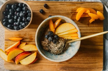 A bowl of almond flour porridge surrounded by fresh fruits. A golden spoon rests to the bottom right of the bowl, and all items sit on top of a wooden cutting board.