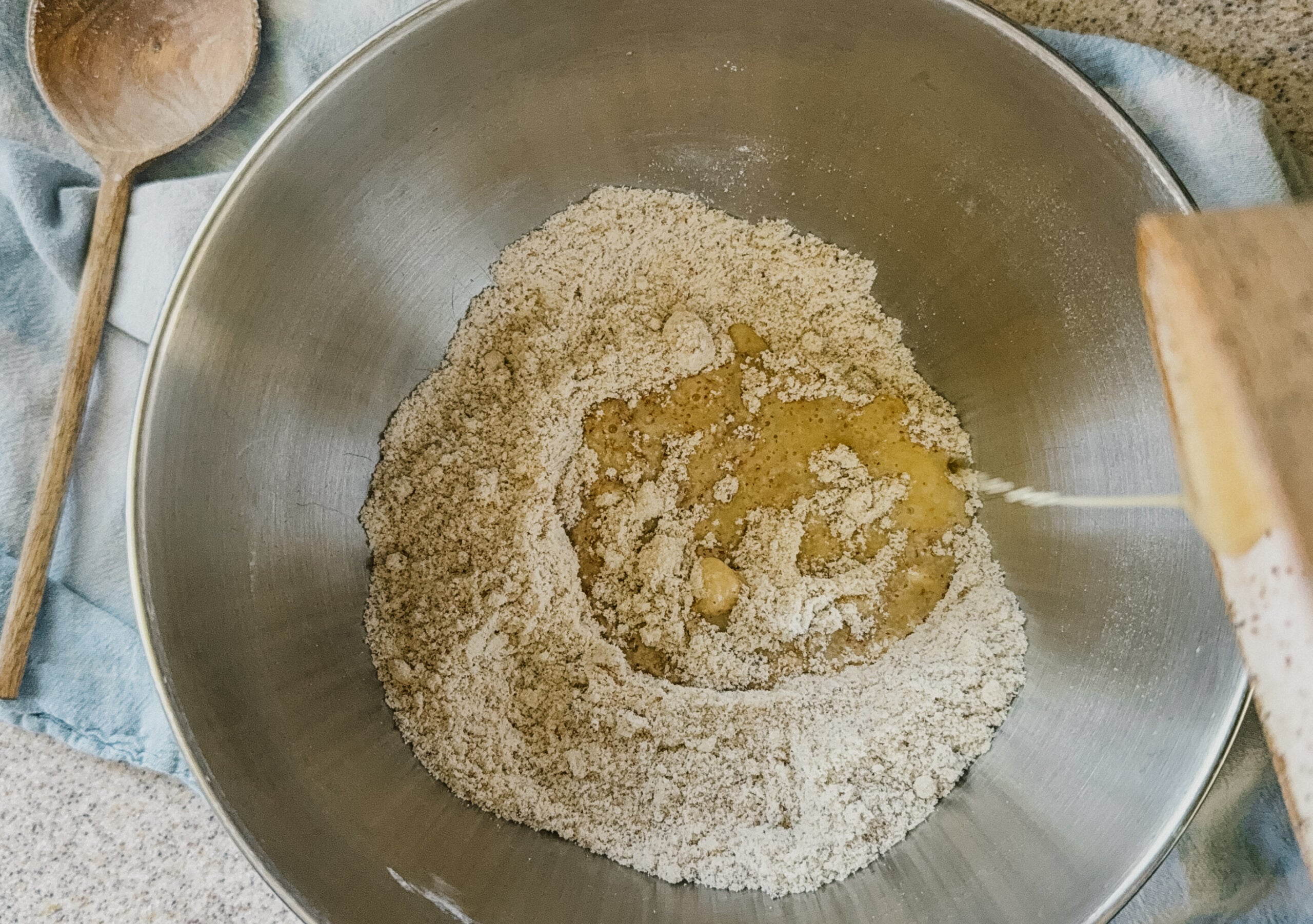 Melted butter being poured from a small bowl into a large silver bowl of dry ingredients.