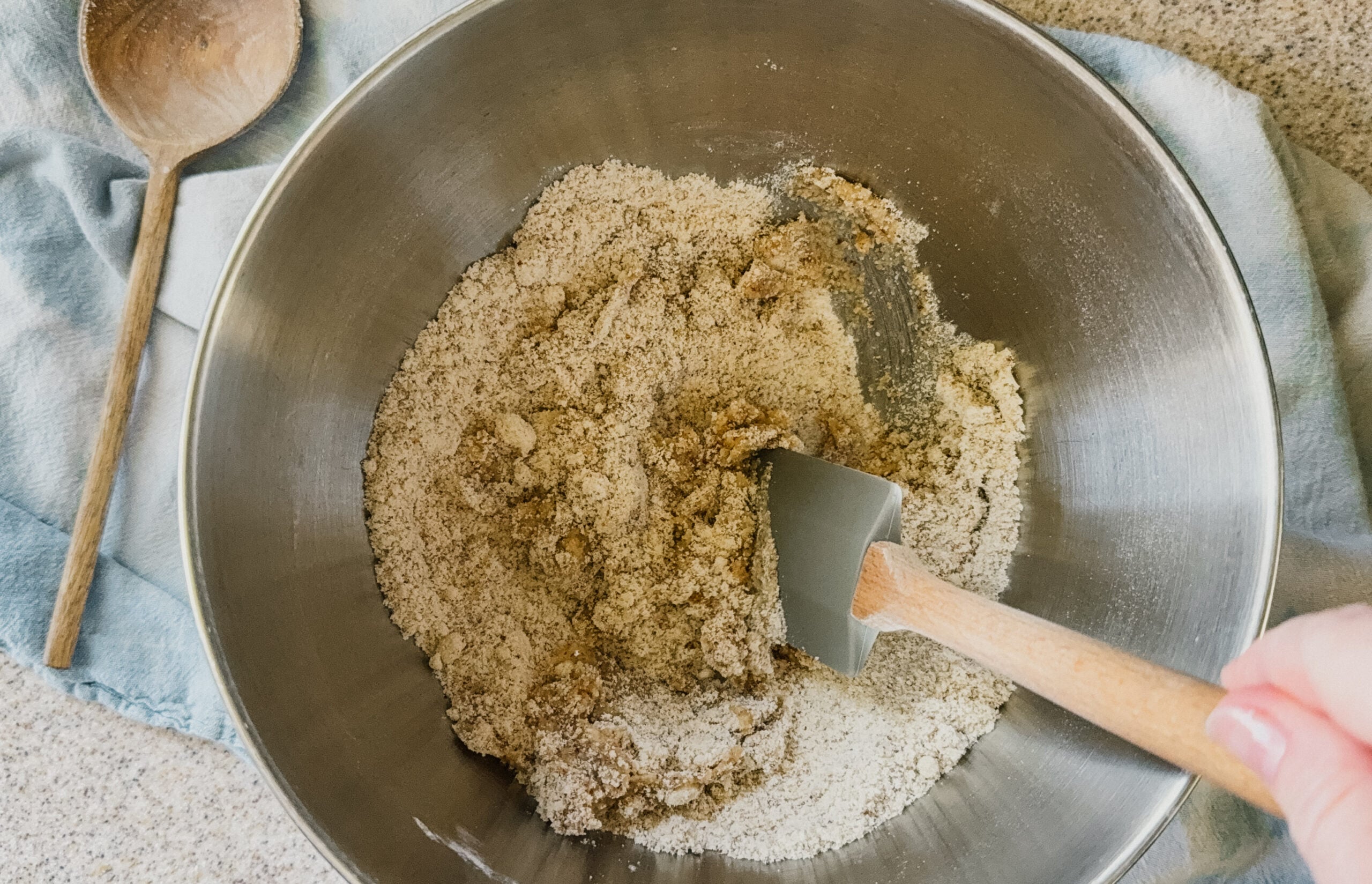A silver bowl with pie crust ingredients being mixed. A spatula sticks out of the lower right side of the bowl.