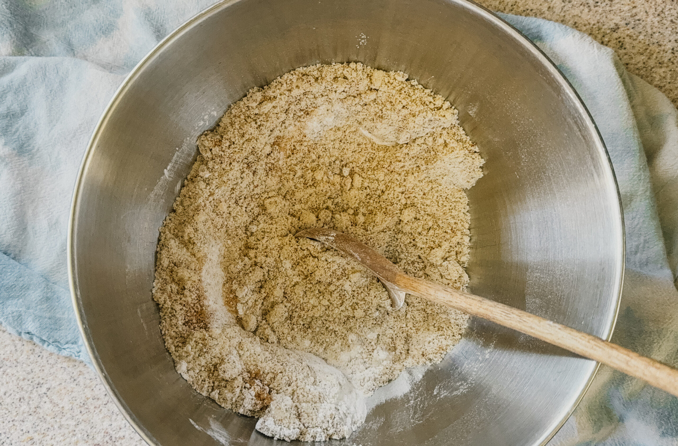 A silver bowl with pie crust ingredients being mixed with a wooden spoon.