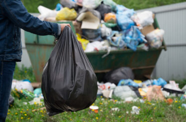 Arm carrying bag of trash to an overflowing dumpster
