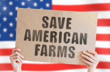The phrase " Save American farms " on a banner in men's hand with blurred American flag on the background. Agriculture business.