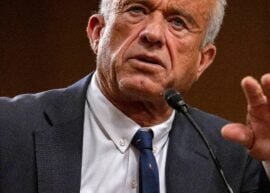 RFK, Jr. in a suit gesturing as he speaks into a microphone