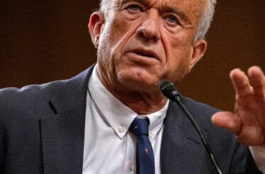 RFK, Jr. in a suit gesturing as he speaks into a microphone