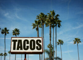 Sign in front of palm trees saying "TACOS"