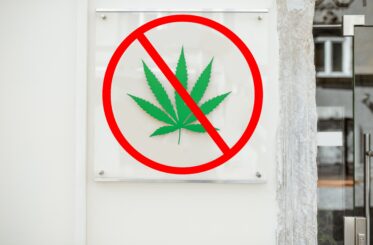 Cannabis shop sign with marijuana leaf on the building wall and "no" sign over it