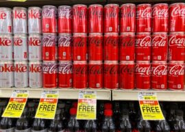 Cans of Coca-Cola products on a shelf with price tags