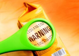 Magnifying glass on food additives label with word warning. Concept warning food additives. Reading ingredients list on food package with magnifying glass.