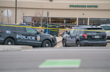 Police officers standing around cars and in front of grocery store