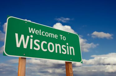 Welcome To Wisconsin Green Road Sign Over Blue Sky with Some Clouds.