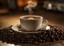 A steaming cup of coffee sitting on top of a pile of coffee beans.