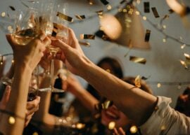 A lively indoor party scene with people toasting champagne glasses amid confetti and warm lights.