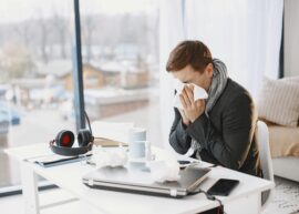 Man sneezing at home desk, indicating remote work during illness.