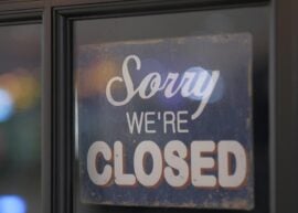 Close-up of a 'Sorry We're Closed' sign on a glass window with bokeh lights in the background.