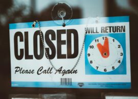 A close-up view of a 'Closed' sign on a door, displaying a return time.