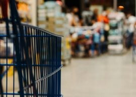 Shopping cart in a busy Brazilian supermarket aisle with blurred background.