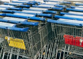 Metallic row of shopping carts with blue handles in a supermarket setting.