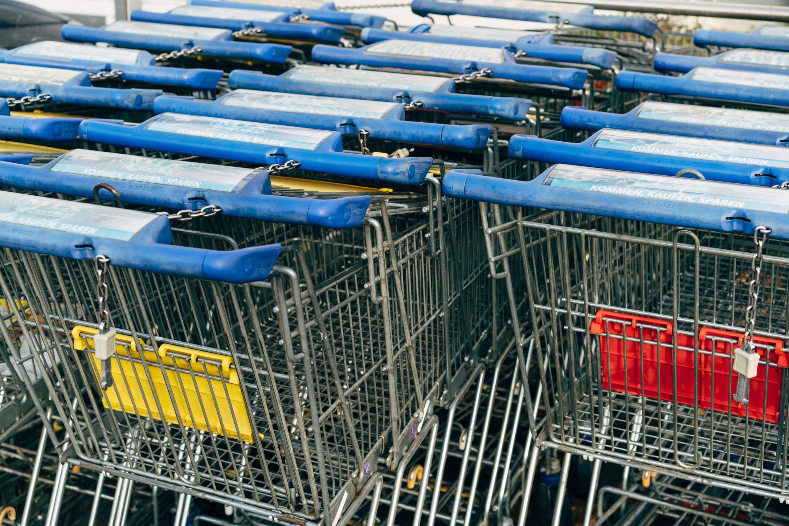 Metallic row of shopping carts with blue handles in a supermarket setting.