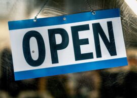 A blue and white open sign hanging on a retail shop's glass door.