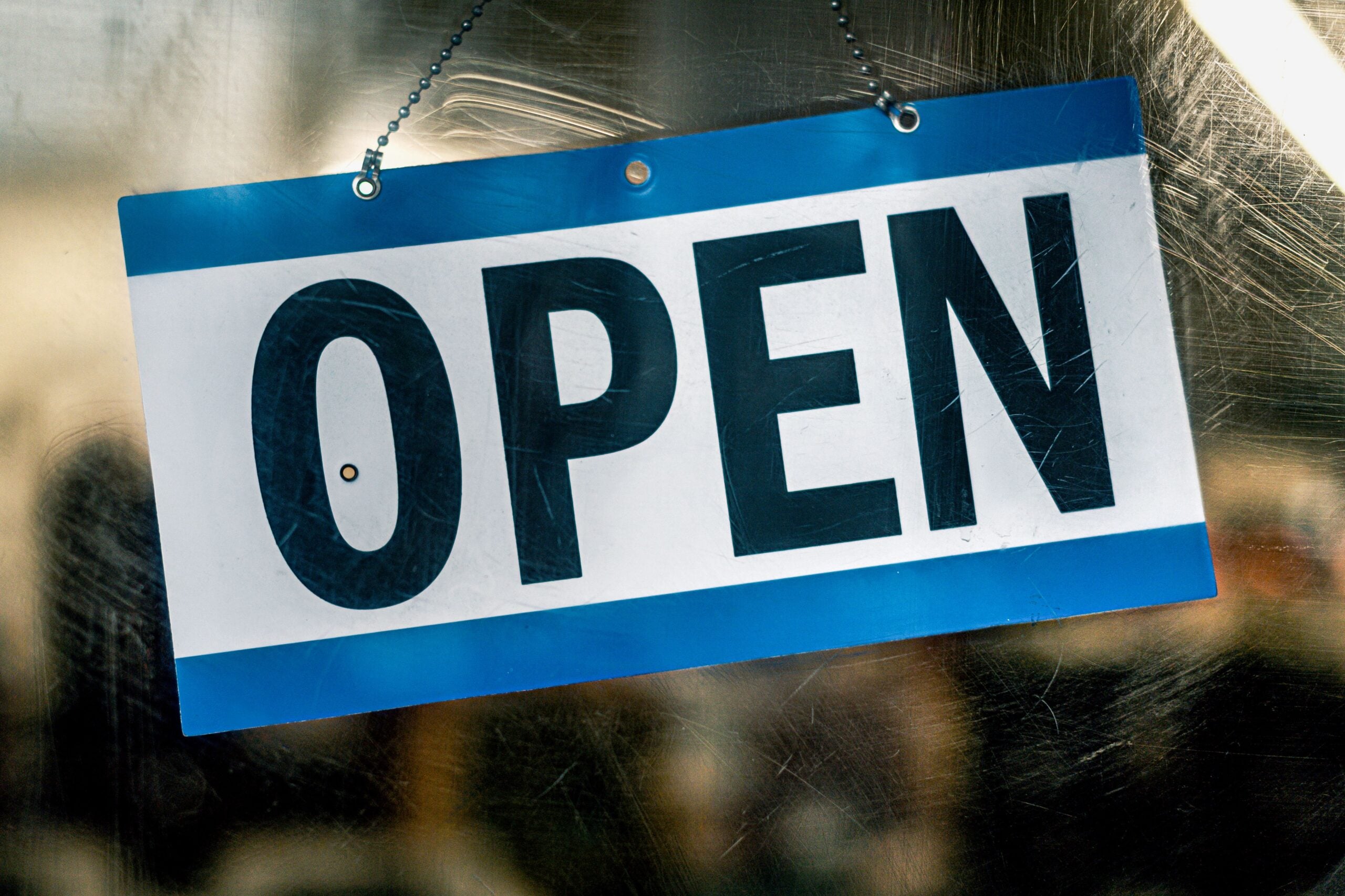 A blue and white open sign hanging on a retail shop's glass door.