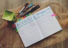 Open food log planner with colorful tabs and pens on a wooden desk, perfect for meal tracking.